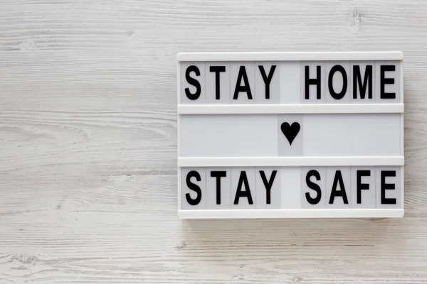 'Stay home stay safe' words on a lightbox on a white wooden background, top view. Overhead, from above, flat lay. Copy space.