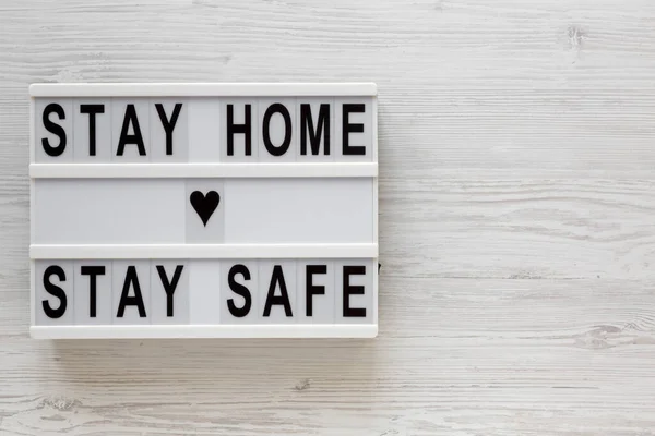 \'Stay home stay safe\' words on a lightbox on a white wooden background, top view. Overhead, from above, flat lay. Space for text.