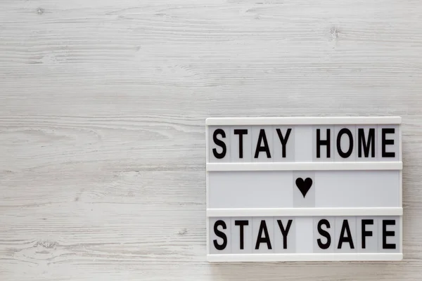 \'Stay home stay safe\' words on a lightbox on a white wooden surface, top view. Overhead, from above, flat lay. Space for text.