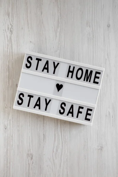 \'Stay home stay safe\' words on a lightbox on a white wooden surface, top view. Overhead, from above, flat lay.
