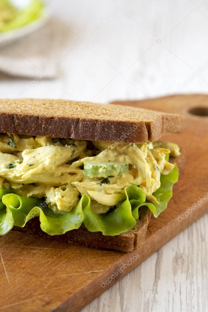 Homemade Coronation Chicken Sandwich on a rustic wooden board on a white wooden background, low angle view. 