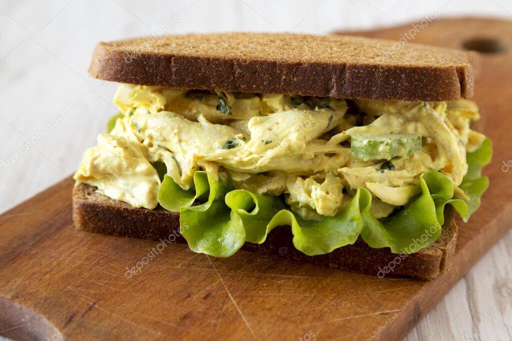 Homemade Coronation Chicken Sandwich on a rustic wooden board on a white wooden background, low angle view. Close-up.