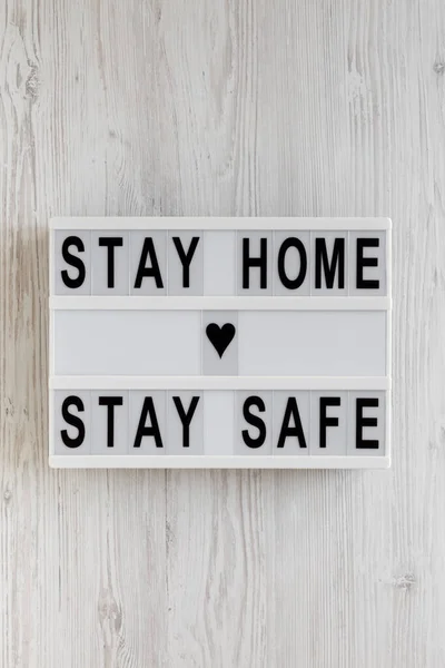 \'Stay home stay safe\' words on a lightbox on a white wooden background, top view. Overhead, from above, flat lay.