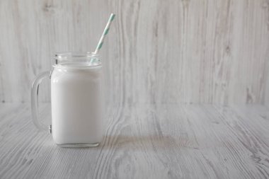 Cam kavanozdaki hindistan cevizi sütü beyaz ahşap arka planda, yan görünüşte. Boşluğu kopyala.