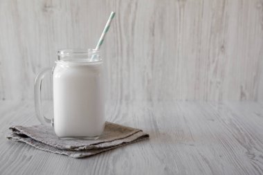 Cam kavanozdaki hindistan cevizi sütü beyaz ahşap bir yüzeyde, yan görünüşte. Metin için boşluk.