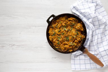 Beyaz ahşap bir masada, dökme demir bir tavada ev yapımı tavuk Tikka Masala, üst manzara. Dümdüz, tepeden, yukarıdan.