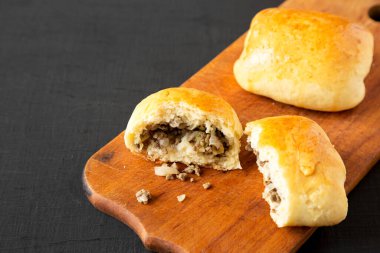 Ev yapımı Rus Bierocks bifteği siyah bir yüzey üzerinde ahşap bir tahta üzerinde, yan görüş. Boşluğu kopyala.