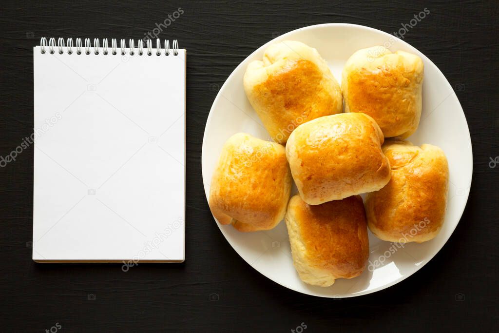 Home-baked Beef Russian Bierocks on a white plate, blank notepad on a black background, top view. Flat lay, overhead, from above. Copy space.
