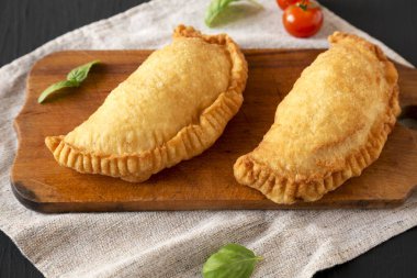 Ev yapımı İtalyan Panzerotti Calzone siyah bir yüzey üzerinde ahşap bir tahta üzerinde, alçak açılı. Yakın plan..