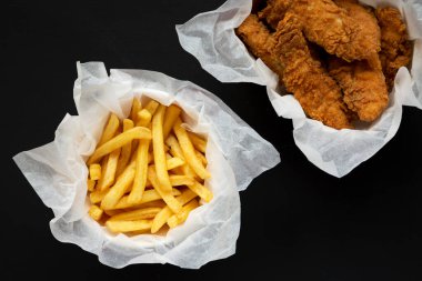 Siyah arka planda patates kızartması ve kızarmış tavuk şeritleri, üst manzara. Tepeden, düz, yukarıdan..