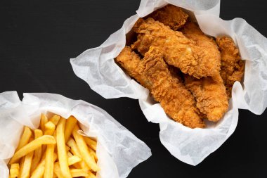 Kızarmış tavuk şeritleri ve patates kızartması. Siyah bir yüzey, üst manzara. Tepeden, düz, yukarıdan..