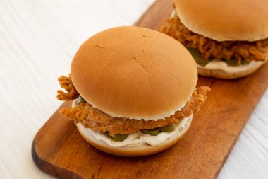 Beyaz ahşap bir masanın üzerinde kızarmış tavuk şeritli ev yapımı hamburgerler. Düşük açılı bir manzara. Yakın plan..