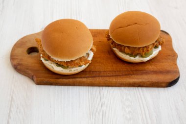 Beyaz ahşap arka planda ahşap bir tahta üzerinde kızarmış tavuk şeritli ev yapımı hamburgerler, yüksek açı manzaralı.. 