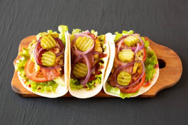 Siyah bir yüzey üzerinde ahşap bir tahta üzerinde ev yapımı çizburgerli taco. Yakın plan..