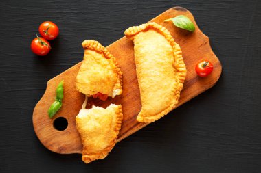 Ev yapımı İtalyan Panzerotti Calzone domates ve mozzarella ile siyah arka planda, ahşap bir tahta üzerinde. Dümdüz, tepeden, yukarıdan. 