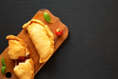 Ev yapımı İtalyan Panzerotti Calzone domates ve mozzarella ile siyah arka planda, ahşap bir tahta üzerinde. Dümdüz, tepeden, yukarıdan. Boşluğu kopyala.