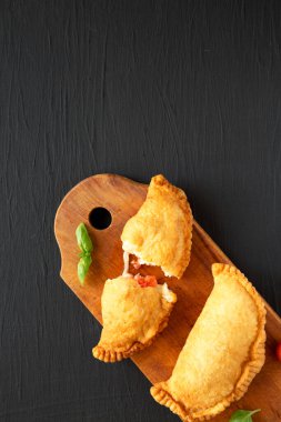 Ev yapımı İtalyan Panzerotti Calzone domates ve mozzarella ile siyah arka planda, ahşap bir tahta üzerinde. Dümdüz, tepeden, yukarıdan. Metin için boşluk.