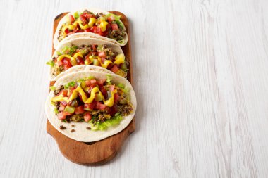 Beyaz ahşap arka planda, düşük açılı, ahşap bir tahtanın üzerinde ev yapımı çizburger tacoları. Metin için boşluk.