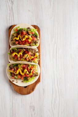 Beyaz ahşap bir yüzey üzerinde ahşap bir tahta üzerinde ev yapımı çizburger tacoları. Dümdüz, tepeden, yukarıdan. Boşluğu kopyala.