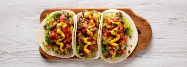 Beyaz ahşap arka planda, ahşap bir tahta üzerinde ev yapımı çizburger tacoları. Dümdüz, tepeden, yukarıdan. 