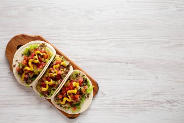 Beyaz ahşap arka planda, ahşap bir tahta üzerinde ev yapımı çizburger tacoları. Dümdüz, tepeden, yukarıdan. Metin için boşluk.