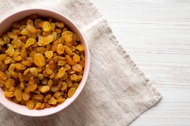 Beyaz ahşap arka planda Pembe Kâse 'de Altın Kuru Üzümler, üst manzara. Dümdüz, tepeden, yukarıdan. Boşluğu kopyala.