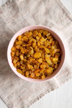 Beyaz ahşap arka planda Pembe Kâse 'de Altın Kuru Üzümler, üst manzara. Dümdüz, tepeden, yukarıdan.