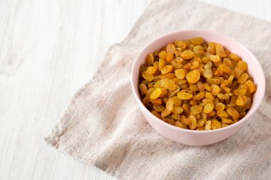 Beyaz ahşap arka planda Pembe Kâse 'de Altın Kuru Üzümler, yan manzara. Boşluğu kopyala.