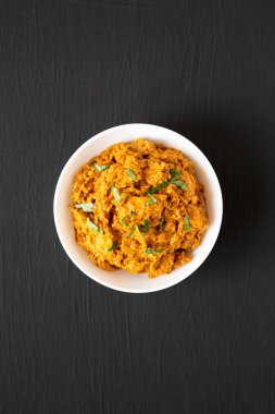 Ev yapımı Tikka Masala tavuğu siyah bir yüzey üzerinde beyaz bir kasede, üst manzara. Dümdüz, tepeden, yukarıdan. 