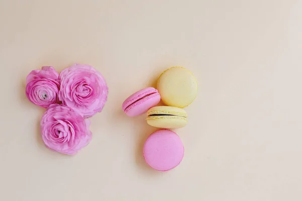 Macaroons and ranunculus on a yellow background. — Stock Photo, Image