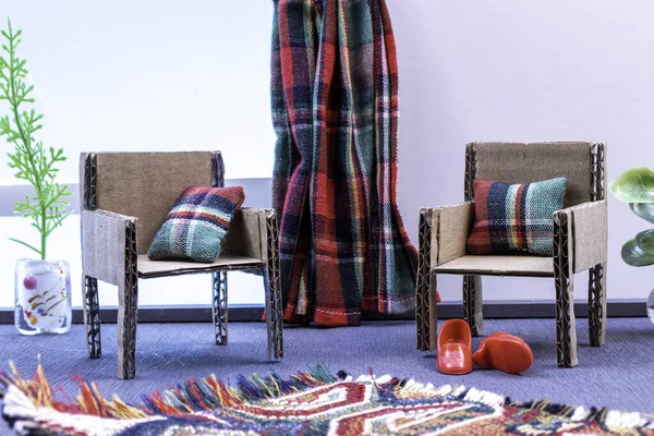 Cardboard miniature furniture for a dollhouse. With checkered pillows and curtains. A rug on the floor.