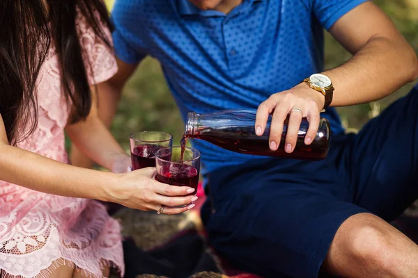 man pouring juice in glass for young woman in summer picnic
