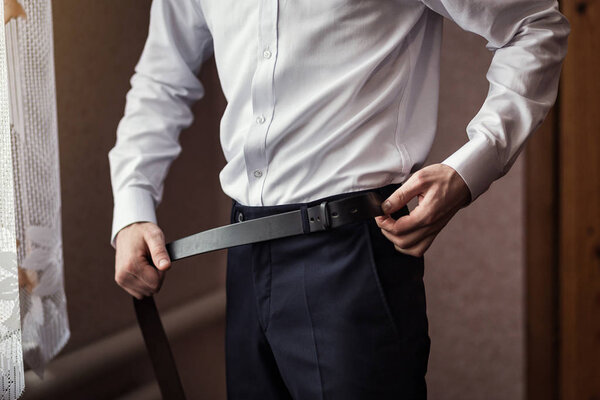 Businessman putting on a belt, fashion and clothing concept,groom getting ready in the morning before ceremony