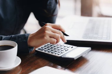 Kadın girişimci, kahve dükkanının mali giderlerini hesaplamak için hesap makinesi kullanıyor..