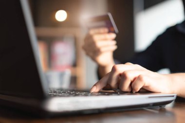 Kadının elleri kredi kartını tutuyor ve online alışveriş için dizüstü bilgisayarın klavyesine yazı yazıyor. Satın almak için öder.