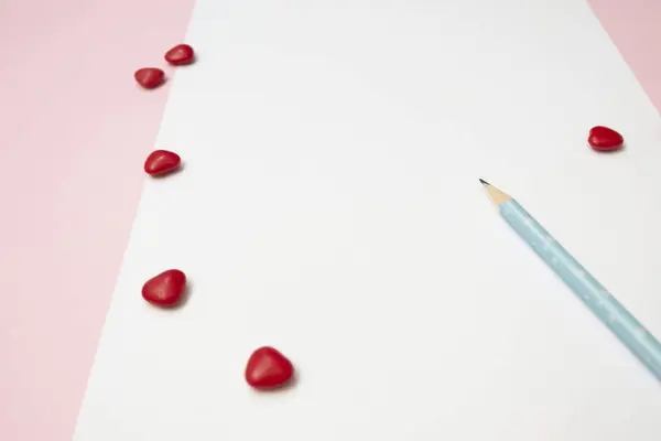 Una nota blanca y un lápiz azul con corazones rojos sobre fondo rosa — Foto de Stock