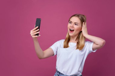 Fotoğraf çekiyorum. Neşeli sarı saçlı kadın izole edilmiş pembe arka planda selfie çekiyor.