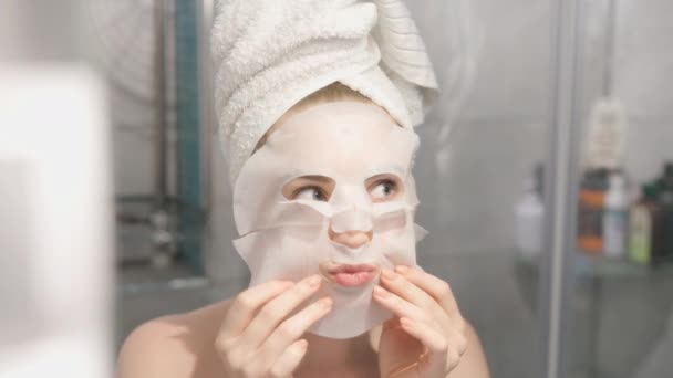 女人在脸上戴着化妆品日本面具 看着镜子 看着浴室里的相机 金发女人 — 图库视频影像