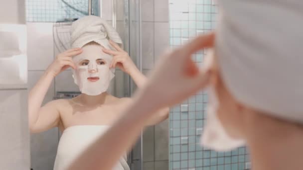 女人在脸上戴着化妆品日本面具 在镜子里看着浴室里的相机 — 图库视频影像