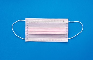 Coronavirus COVID-19 salgını. Korona virüsüne karşı korunmak için antiviral tıbbi maske. Cerrahi koruyucu maske. Beyaz arka planda tıbbi solunum bandajı var. Karantina, evde kal. mavi arkaplan