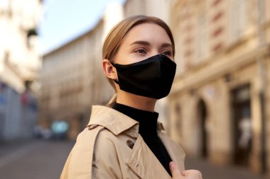 Coronavirus salgını karantinası sırasında moda kıyafeti giyen bir kadın. Model gibi giyinmiş, el yapımı bir yüz maskesi. Boş caddede yürüyen bir turist. Moda koruyucu maskeli güzel sarışın kadın. Mimarlık geçmişi. Sokak