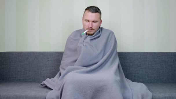 毛布で覆われた病気の男は温度を測定し 結果に驚いています 若い男の発熱を動揺 急性呼吸器ウイルス感染症 風邪のインフルエンザ自宅での自己投薬 4K映像 — ストック動画