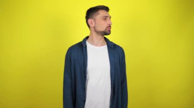 Mavi tişörtlü ve beyaz tişörtlü genç bir adam etrafa mesajlaşmak için bakıyor. Kopyalama alanı olan sarı arkaplan. 4k yavaş çekim görüntüsü