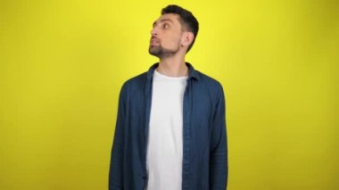 Mavi tişörtlü ve beyaz tişörtlü genç bir adam mesaj ve omuz silkme için etrafa bakıyor. Kopyalama alanı olan sarı arkaplan. 4k yavaş çekim görüntüsü