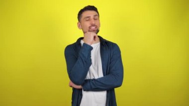 Mavi tişörtlü ve beyaz tişörtlü genç bir adam etrafa mesajlaşmak için bakıyor. Kopyalama alanı olan sarı arkaplan. 4k yavaş çekim görüntüsü