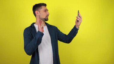Mavi tişörtlü ve beyaz tişörtlü genç bir blog yazarı akıllı telefondan yayın yapıyor. Kopyalama alanı olan sarı arkaplan. 4k yavaş çekim görüntüsü