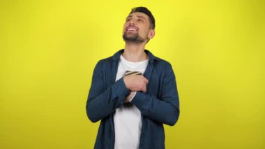 Beyaz tişörtlü genç bir adam hediyeli bir kutuya sarılıyor, kameraya bakıyor ve gülümsüyor, sarı arkaplan. Tatil konsepti: Yeni yıl, Noel, Aziz Nicholas Günü, Sevgililer Günü, doğum günü. 4k görüntü