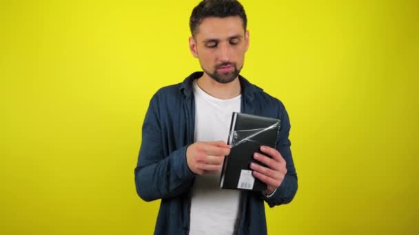 Молодой Человек Синей Рубашке Белой Футболке Распаковывает Новый Черный Блокнот — стоковое видео
