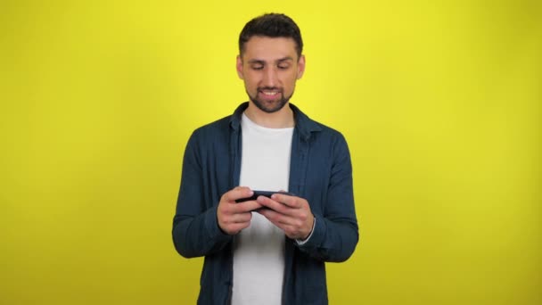 Молодой Человек Синей Рубашке Белой Футболке Энтузиазмом Играет Игру Смартфоне — стоковое видео