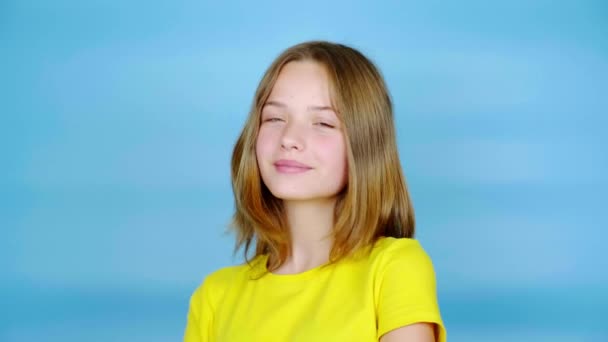 黄色のTシャツを着た幸せな10代の女の子がポーズをとってカメラを見ている コピースペース付きの青の背景 10代の感情4K映像 — ストック動画